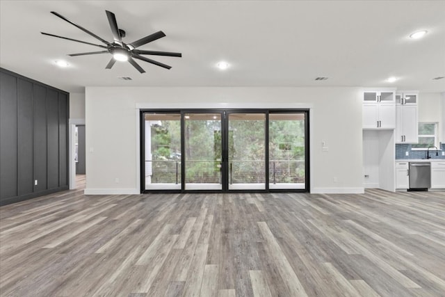 unfurnished living room featuring plenty of natural light, ceiling fan, light wood-type flooring, and sink