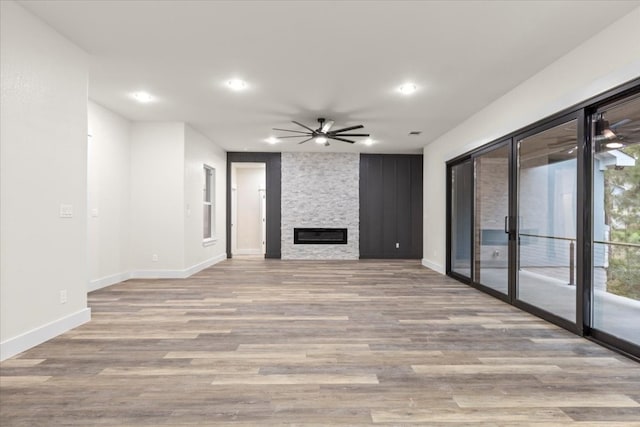 unfurnished living room featuring ceiling fan, a stone fireplace, and light wood-type flooring