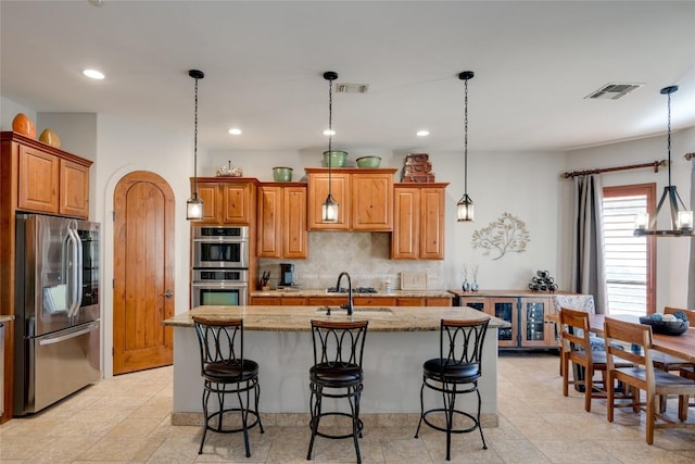 kitchen featuring a kitchen island with sink, light stone countertops, pendant lighting, and stainless steel appliances