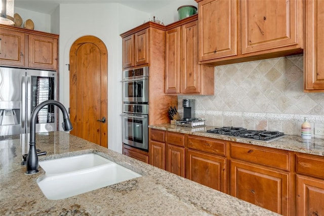 kitchen with stainless steel appliances, light stone countertops, sink, and decorative backsplash