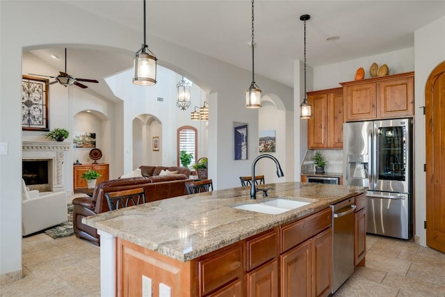 kitchen with stainless steel appliances, an island with sink, sink, and light stone counters