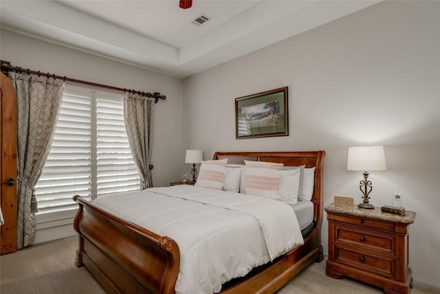 bedroom featuring multiple windows, a raised ceiling, and light carpet