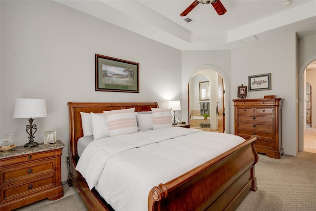 carpeted bedroom featuring ceiling fan, ensuite bathroom, and a tray ceiling