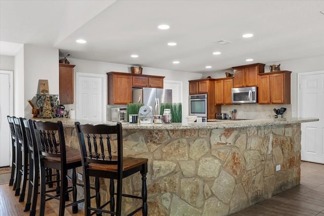 133 Blue Jack Oak Ln, Bastrop, TX 78602 - kitchen with appliances with stainless steel finishes, a breakfast bar, recessed lighting, brown cabinetry, and tasteful backsplash