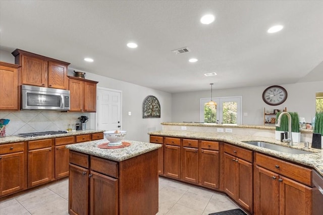 kitchen featuring hanging light fixtures, backsplash, appliances with stainless steel finishes, brown cabinetry, and a sink