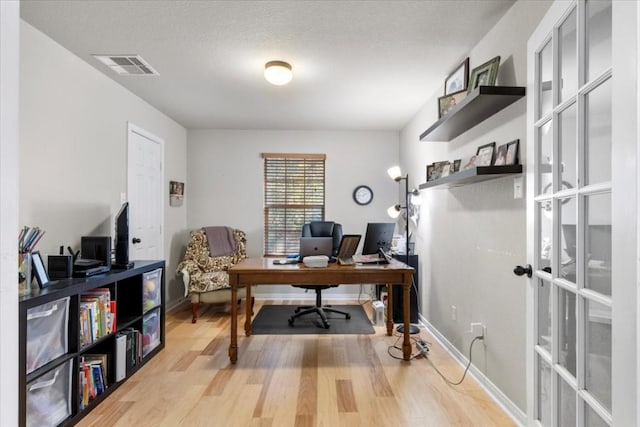 office area featuring light wood finished floors, baseboards, visible vents, and a textured ceiling