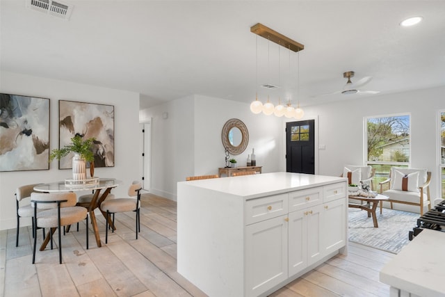 kitchen featuring light hardwood / wood-style flooring, ceiling fan, decorative light fixtures, a kitchen island, and white cabinetry