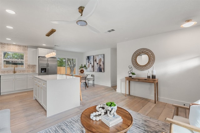 kitchen with a center island, white cabinets, stainless steel refrigerator with ice dispenser, hanging light fixtures, and light wood-type flooring