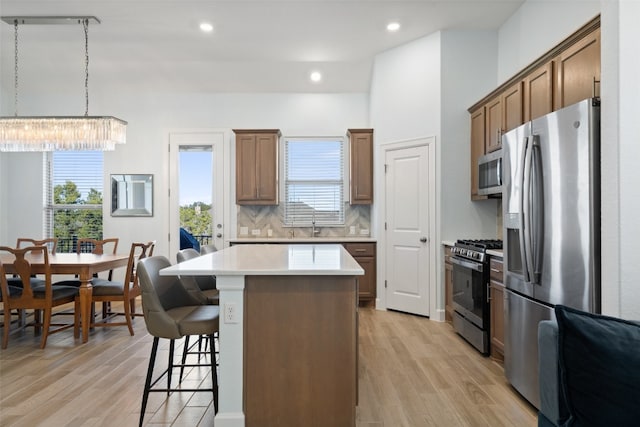 kitchen featuring a center island, stainless steel appliances, decorative light fixtures, and light hardwood / wood-style flooring