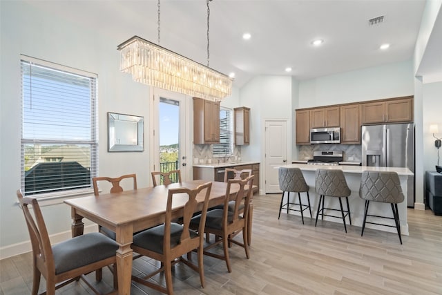 dining space featuring light hardwood / wood-style flooring, high vaulted ceiling, and a notable chandelier