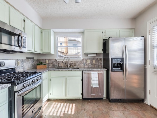 kitchen with sink, a textured ceiling, appliances with stainless steel finishes, light stone countertops, and backsplash