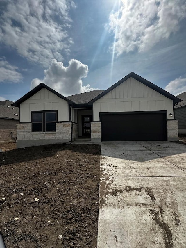 view of front of property with driveway, stone siding, roof with shingles, board and batten siding, and an attached garage