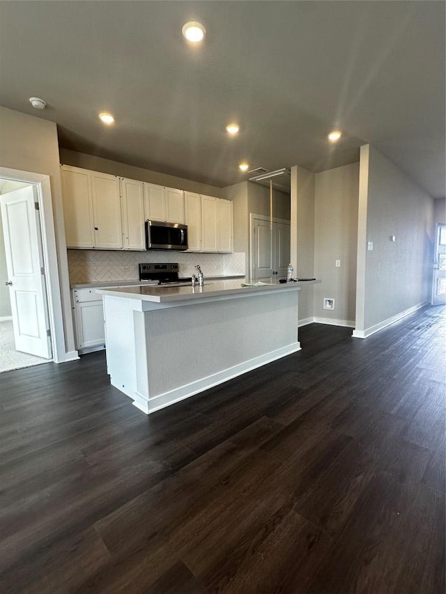 kitchen with backsplash, dark wood-type flooring, an island with sink, white cabinets, and stainless steel appliances