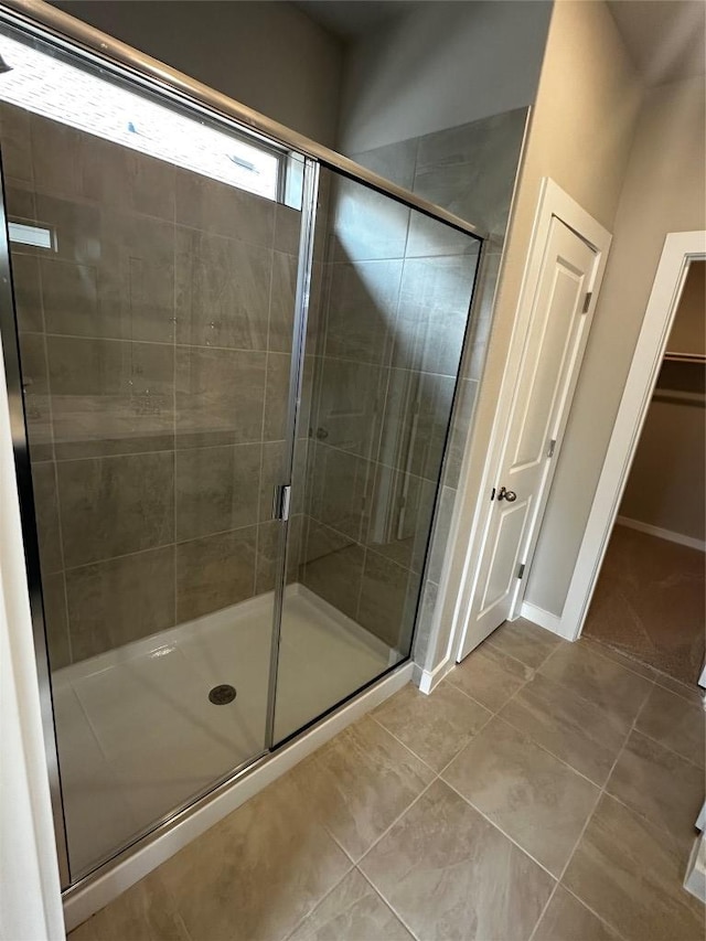 bathroom with a walk in closet, a shower stall, baseboards, and tile patterned floors