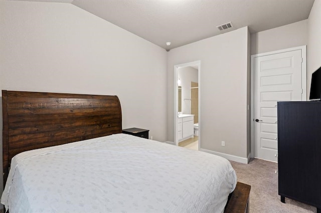 carpeted bedroom featuring ensuite bath and vaulted ceiling