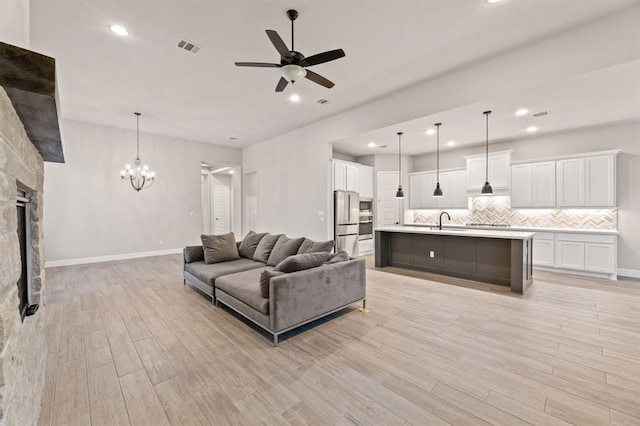 living room with ceiling fan with notable chandelier, light hardwood / wood-style floors, a stone fireplace, and sink