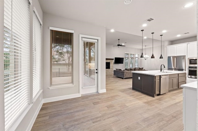 kitchen featuring sink, light hardwood / wood-style floors, decorative light fixtures, a center island with sink, and appliances with stainless steel finishes