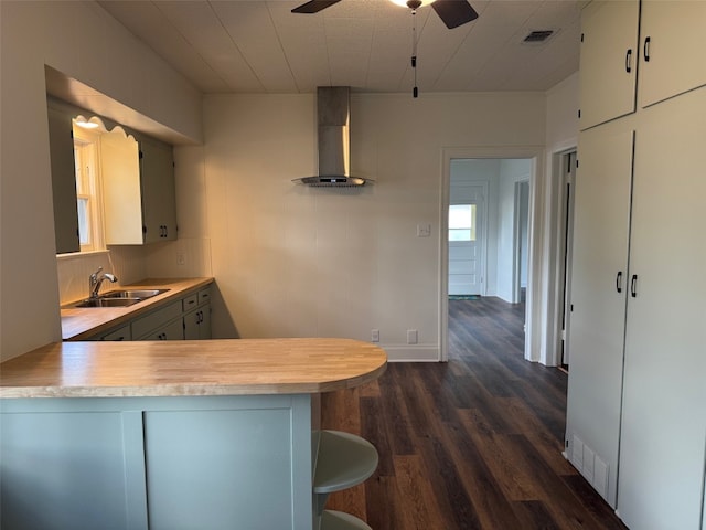 kitchen featuring sink, wall chimney exhaust hood, ceiling fan, dark hardwood / wood-style flooring, and kitchen peninsula