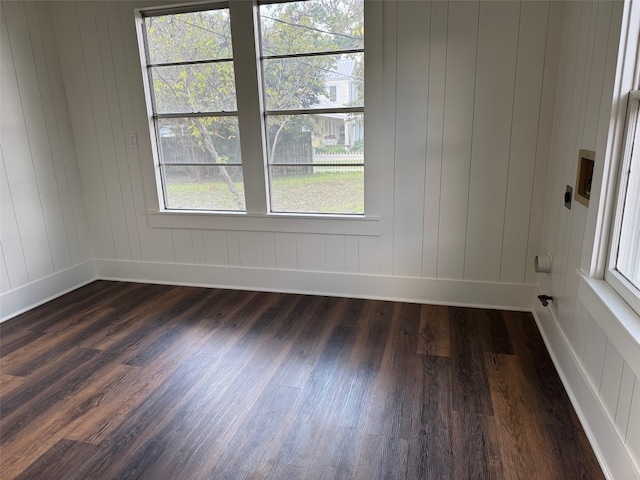 unfurnished room featuring plenty of natural light, dark wood-type flooring, and wooden walls