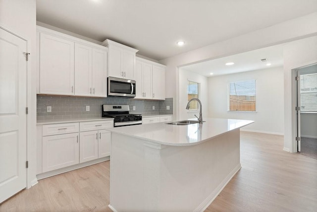 kitchen with a center island with sink, sink, light hardwood / wood-style flooring, white cabinetry, and stainless steel appliances