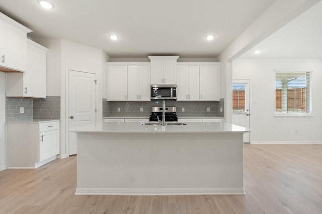 kitchen featuring appliances with stainless steel finishes, sink, a center island with sink, white cabinets, and light hardwood / wood-style floors