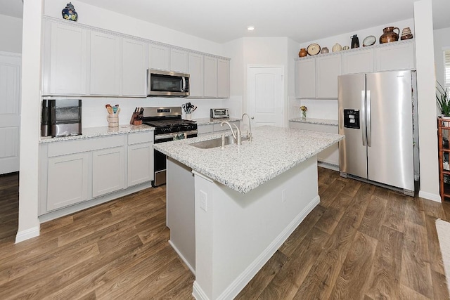 kitchen with dark hardwood / wood-style floors, an island with sink, sink, light stone counters, and stainless steel appliances