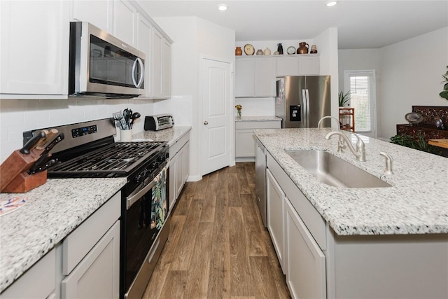 kitchen with sink, hardwood / wood-style floors, stainless steel appliances, light stone countertops, and an island with sink