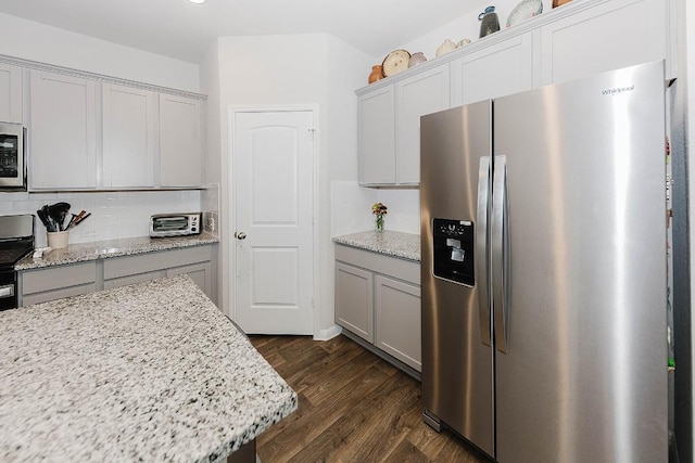 kitchen with gray cabinets, appliances with stainless steel finishes, dark hardwood / wood-style floors, tasteful backsplash, and light stone counters