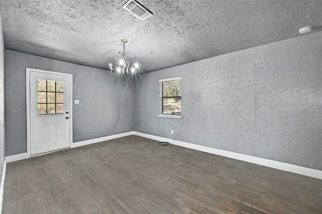 empty room with dark hardwood / wood-style floors, a healthy amount of sunlight, and an inviting chandelier