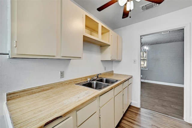 kitchen with cream cabinetry, ceiling fan with notable chandelier, light hardwood / wood-style flooring, and sink