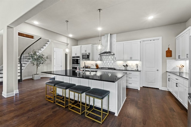 kitchen with wall chimney range hood, a breakfast bar area, white cabinetry, stainless steel appliances, and decorative light fixtures