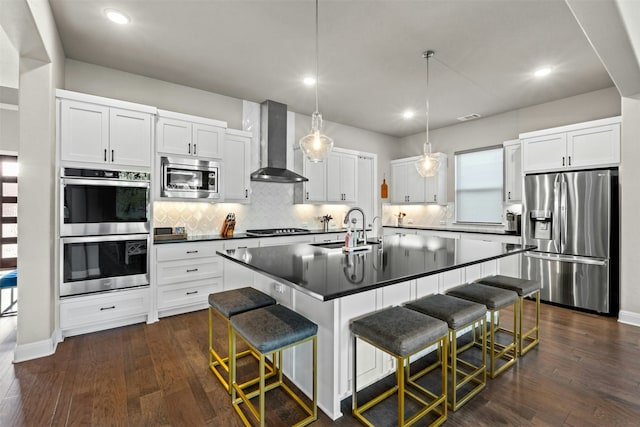 kitchen with appliances with stainless steel finishes, a breakfast bar, decorative light fixtures, sink, and wall chimney range hood