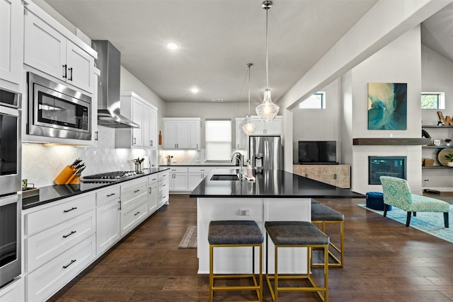 kitchen with wall chimney exhaust hood, sink, a center island with sink, appliances with stainless steel finishes, and a kitchen breakfast bar