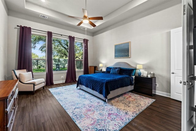 bedroom featuring dark hardwood / wood-style flooring, a tray ceiling, and ceiling fan