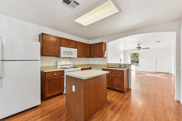 kitchen with ceiling fan, kitchen peninsula, white appliances, a kitchen island, and light wood-type flooring