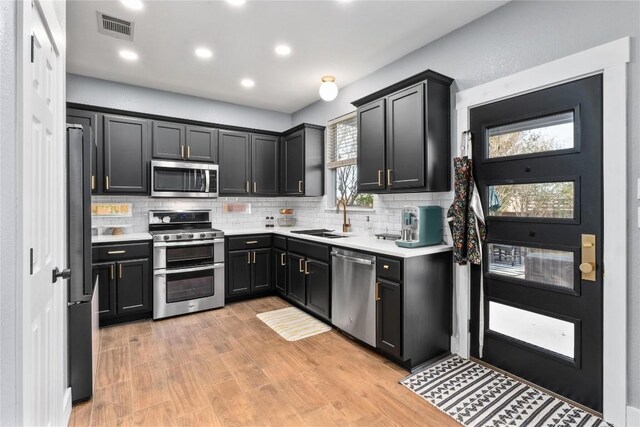 kitchen featuring stainless steel appliances, light hardwood / wood-style floors, backsplash, and sink