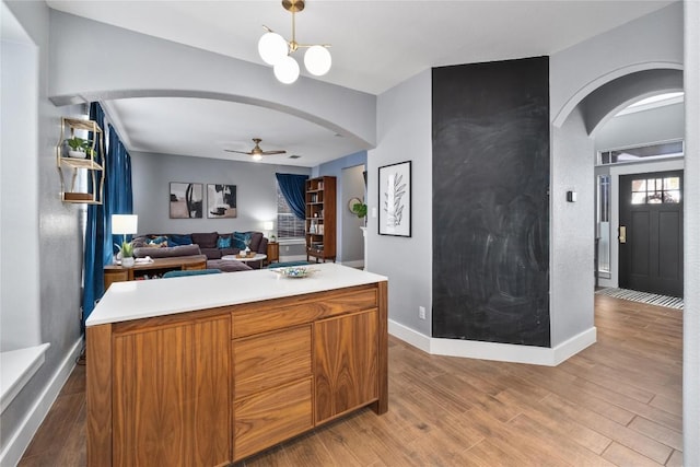 kitchen with pendant lighting, ceiling fan with notable chandelier, wood-type flooring, and a center island