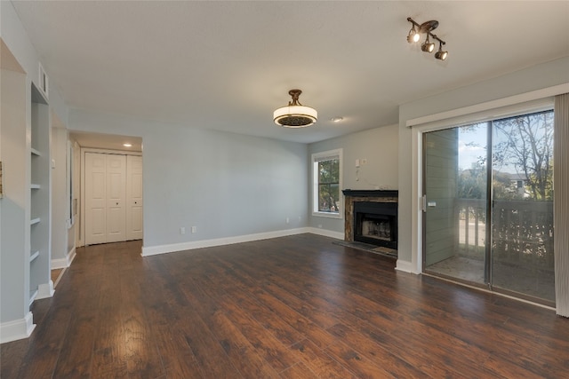 unfurnished living room featuring built in shelves, dark hardwood / wood-style flooring, and a healthy amount of sunlight