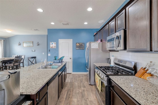 kitchen featuring dark brown cabinetry, light stone counters, light hardwood / wood-style floors, and appliances with stainless steel finishes