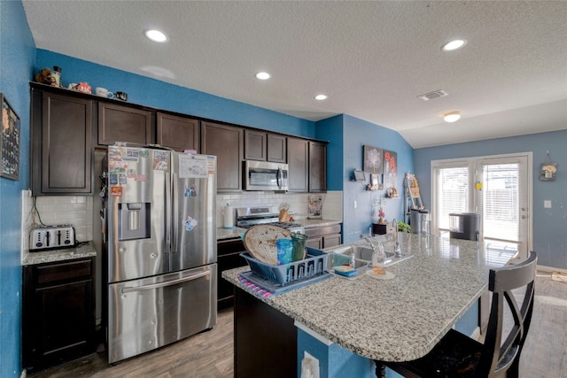 kitchen with appliances with stainless steel finishes, a textured ceiling, wood-type flooring, lofted ceiling, and an island with sink