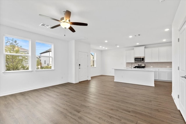 unfurnished living room featuring a wealth of natural light, ceiling fan, and dark hardwood / wood-style floors