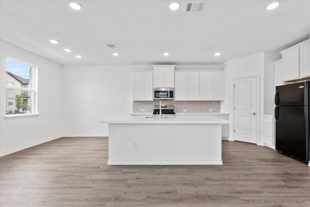 kitchen with sink, stainless steel appliances, a center island with sink, white cabinets, and light wood-type flooring