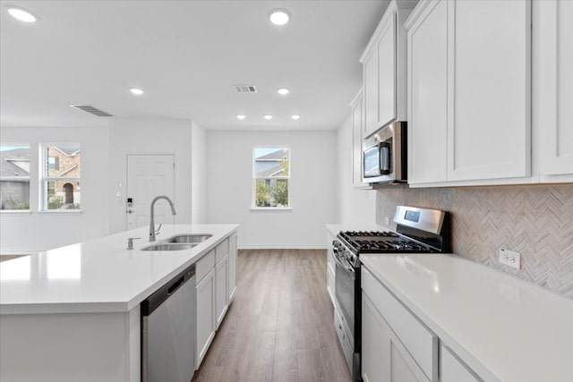 kitchen featuring decorative backsplash, appliances with stainless steel finishes, a kitchen island with sink, sink, and white cabinets