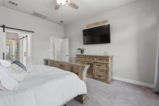 bedroom with a barn door, ceiling fan, ensuite bathroom, and light colored carpet