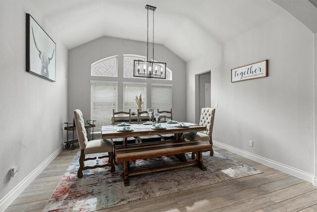 dining area with a chandelier, vaulted ceiling, and light hardwood / wood-style flooring