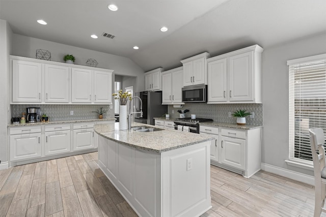 kitchen featuring light stone counters, white cabinets, an island with sink, and appliances with stainless steel finishes