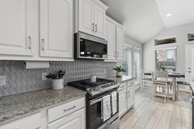 kitchen featuring white cabinets, vaulted ceiling, light stone countertops, tasteful backsplash, and stainless steel appliances