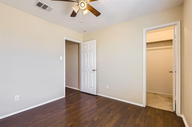 unfurnished bedroom featuring dark hardwood / wood-style flooring, a closet, a spacious closet, and ceiling fan