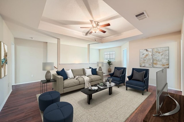 living room with a raised ceiling, ceiling fan, crown molding, and dark wood-type flooring