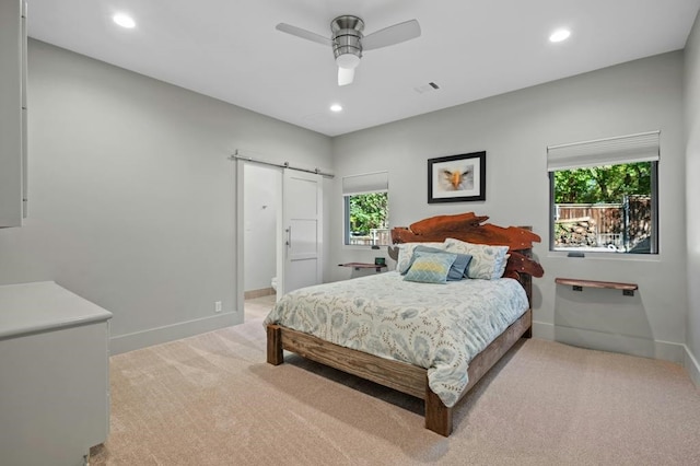 bedroom featuring ceiling fan, a barn door, light carpet, and ensuite bath